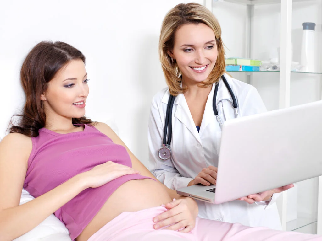 Pregnant woman consulting with her doctor, who is reviewing information on a laptop